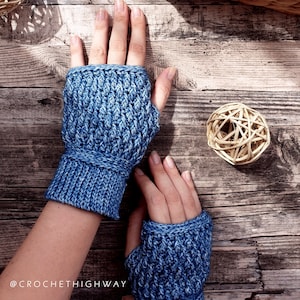 May include: A pair of blue fingerless gloves with a textured knit pattern. The gloves are shown on a wooden surface with a woven ball.