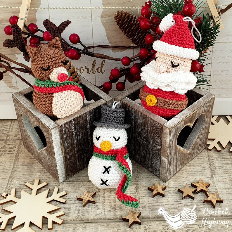 Peut inclure: Trois ornements de No&euml;l en crochet&nbsp;: un renne, le p&egrave;re No&euml;l et un bonhomme de neige. Les ornements sont pr&eacute;sent&eacute;s dans des bo&icirc;tes en bois avec des d&eacute;coupes en forme de c&oelig;ur. Les ornements sont tous blancs avec des accents color&eacute;s.
