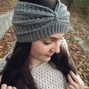 May include: Gray crochet headband with a knotted detail on top. The headband is worn by a person with long dark hair.