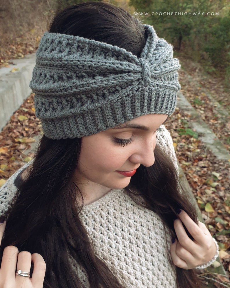 May include: Gray crochet headband with a knotted detail on top. The headband is worn by a person with long dark hair.
