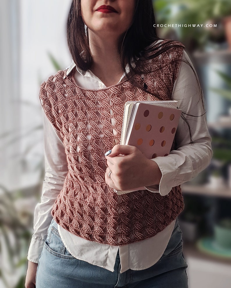 K&ouml;nnte beinhalten: Eine rosa geh&auml;kelte Weste mit einem wei&szlig;en Hemd darunter und blauen Jeans. Die Weste hat ein Spitzenmuster und wird von einer Person getragen, die zwei Notizb&uuml;cher h&auml;lt.