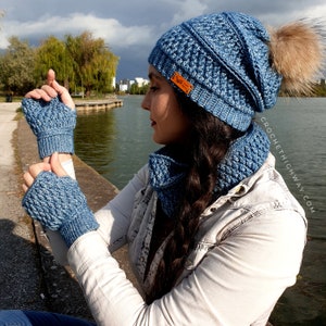 May include: A blue crocheted hat, scarf and fingerless gloves set. The hat has a pompom on top and the scarf is a cowl style. The set is made with a textured stitch.