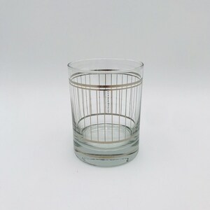 May include: A clear glass tumbler with a silver geometric pattern. The glass has a wide base and straight sides.