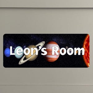 May include: A black and blue space-themed door sign with planets and stars. The sign reads "Leon's Room".