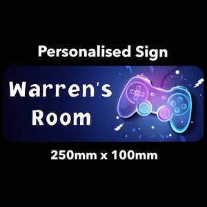 May include: A personalised room sign featuring a neon blue and pink video game controller graphic. The sign reads "Warren's Room" and measures 250mm x 100mm.
