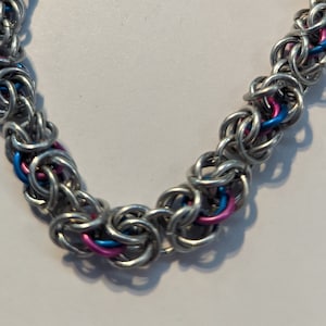 May include: A silver chain bracelet with pink and blue accents. The bracelet is made of small metal rings linked together.
