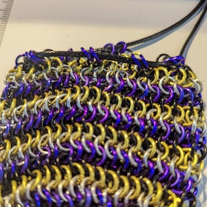 May include: A small, chainmail bag with a black drawstring. The chainmail is made of silver, gold, and purple metal rings.