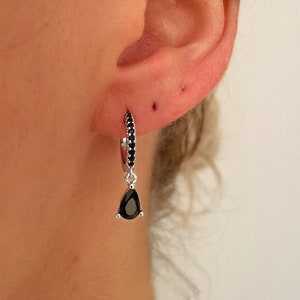 May include: A pair of silver hoop earrings with black stones. The hoop earrings have a small black teardrop-shaped stone dangling from the bottom.