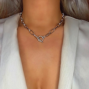 May include: A silver chain necklace with a toggle clasp. The chain is made of thick, oval-shaped links.