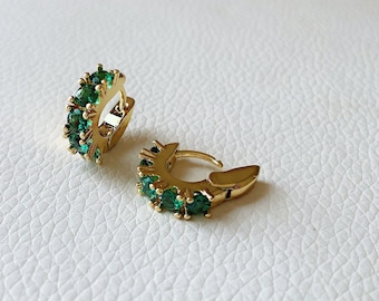 May include: A pair of gold hoop earrings with green gemstones. The earrings are small and delicate.