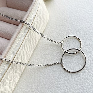 May include: A silver chain necklace with two interlocking circles as a pendant.