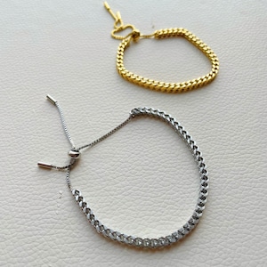 May include: Two adjustable chain bracelets, one gold and one silver, with a curb chain design.