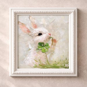 Peut inclure: Tableau encadré blanc représentant un lapin blanc aux oreilles roses, mangeant un trèfle à quatre feuilles vert. La peinture a une palette de couleurs pastel et un style impressionniste texturé. Une charmante représentation de la nature.