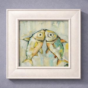 May include: Square framed artwork featuring two stylized fish kissing. The fish are painted in shades of yellow, green, and blue, with large, expressive eyes. The artwork is set against a light, textured background, and framed in a white square frame.