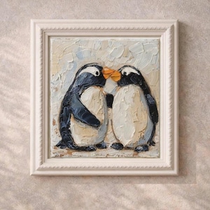 May include: An oil painting featuring two penguins with black and white plumage and orange beaks, rendered with thick, textured impasto brushstrokes. The artwork is enclosed in a decorative, off-white wooden frame with a detailed border.