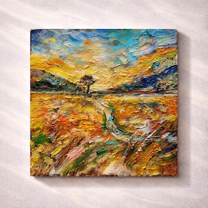 May include: A square oil painting featuring a thick impasto texture. The landscape depicts a golden field under a vibrant sky with shades of yellow, orange, and blue. A single dark tree stands in the center, with a winding path leading through the textured, multi-colored terrain toward the horizon.