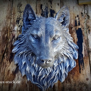 Könnte beinhalten: Eine detaillierte, graue Wolfskopfskulptur mit aufwendigen Fellzeichnungen. Die Skulptur ist auf einer verwitterten Holzoberfläche montiert. Die Augen des Wolfes sind fokussiert, und der Gesamteffekt ist realistisch. Die Website-Adresse "www.lux-stuck.de" ist unten sichtbar.