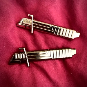 Puede incluir: Dos juguetes de sable de luz de metal de color dorado. Los sables de luz tienen un diseño detallado con una serie de líneas y crestas.