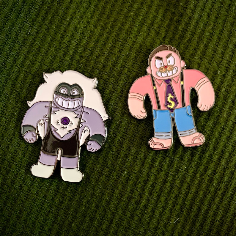 May include: Two enamel pins featuring cartoon characters. The first pin is purple and white and depicts a character with a purple gemstone on their chest. The second pin is pink, blue, and white and depicts a character with a pink shirt and blue pants.