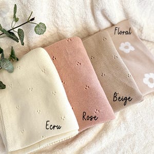 May include: Four knitted baby blankets in different colors: ecru, rose, beige, and floral. The blankets have a delicate floral pattern and are arranged in a stack.