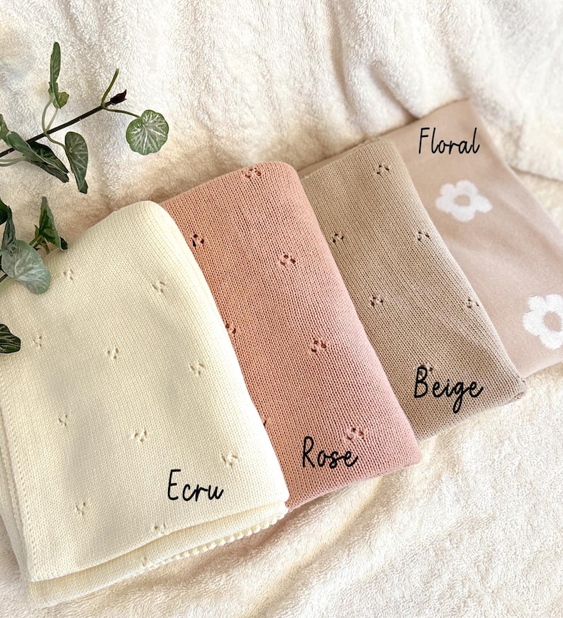 May include: Four knitted baby blankets in different colors: ecru, rose, beige, and floral. The blankets have a delicate floral pattern and are arranged in a stack.