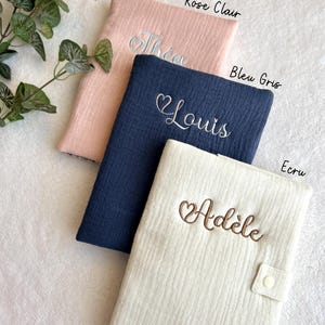 May include: Three personalized baby blankets in different colors: pink, blue, and cream. The blankets are made of a soft, textured fabric and feature embroidered hearts and names: Thea, Louis, and Ad&egrave;le.