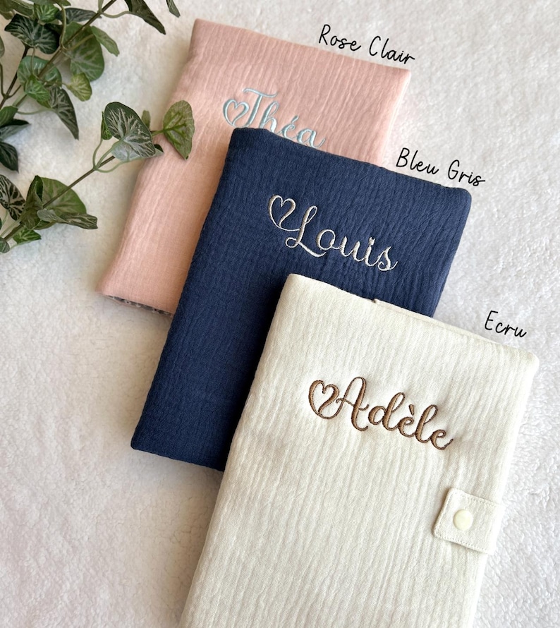 May include: Three personalized baby blankets in different colors: pink, blue, and cream. The blankets are made of a soft, textured fabric and feature embroidered hearts and names: Thea, Louis, and Ad&egrave;le.