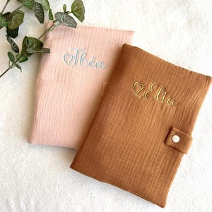 May include: Two personalized baby bibs, one pink with the name "Th&eacute;a" embroidered in white and one brown with the name "Elia" embroidered in gold.