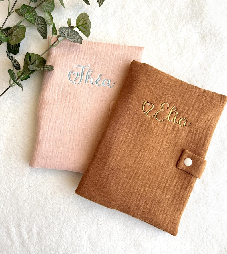 May include: Two personalized baby bibs, one pink with the name "Th&eacute;a" embroidered in white and one brown with the name "Elia" embroidered in gold.