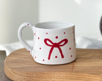 Handmade stoneware mug featuring a delicate hand painted red bow