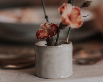 May include: A small white ceramic vase with a simple design holds a bouquet of dried pink and orange flowers.