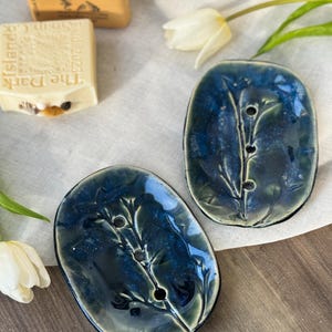 Puede incluir: Dos jaboneras de cerámica azul con un diseño floral. Las jaboneras tienen un esmalte azul claro con un patrón floral azul oscuro.