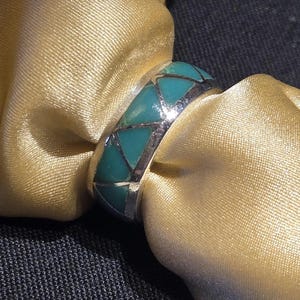May include: A silver ring with a turquoise inlay. The turquoise is set in a geometric pattern.