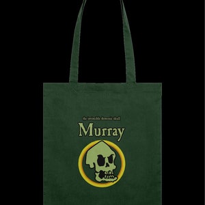 Può includere: Una borsa di tela verde con un'immagine di teschio e il testo "the invincible demonic skull Murray".