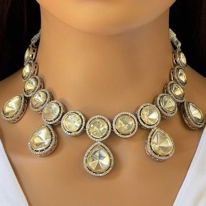 May include: A silver and white necklace with teardrop-shaped stones and a matching pair of earrings. The necklace has a delicate design with small stones surrounding the larger teardrop stones.
