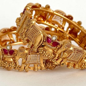 May include: Two gold bangles with intricate elephant designs and red and white gemstones.
