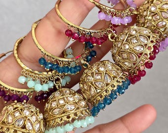 May include: Gold-toned hoop earrings with dangling beaded accents in various colors, including purple, red, blue, and mint green. The earrings feature intricate, jewel-encrusted bell-shaped dangles. The earrings are designed with a traditional aesthetic.