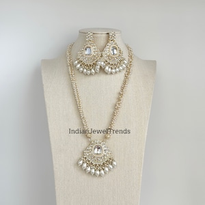 May include: A gold and white pearl necklace and earrings set with a large, clear, faceted stone pendant. The necklace has two strands of pearls and the pendant is surrounded by smaller pearls.