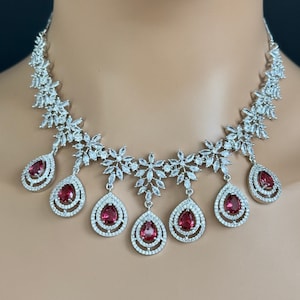 Puede incluir: Un collar de plata con un diseño floral y piedras rojas en forma de lágrima colgantes.