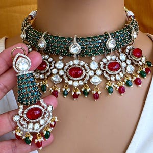 Puede incluir: Un conjunto de collar y pendientes adornado con piedras preciosas de color verde esmeralda y rojo rubí. El collar es de estilo gargantilla con una base de cuentas verdes y grandes piedras transparentes en forma de lágrima. Los pendientes tienen un diseño a juego.
