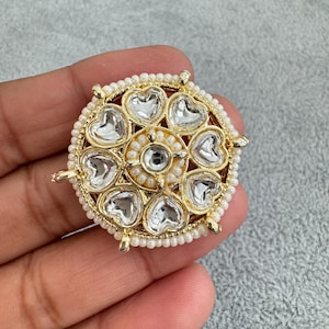 May include: A gold-toned, round, decorative piece with a design of white heart-shaped stones surrounded by white pearls.