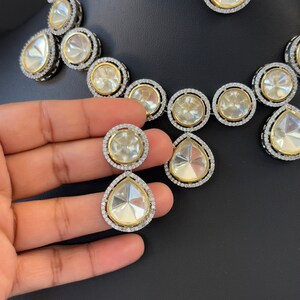 May include: A silver and gold necklace and earrings set with large clear stones. The necklace has a teardrop shape and the earrings are round.