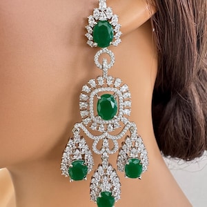 Può includere: Eleganti orecchini a lampadario con grandi pietre preziose verde smeraldo ovali circondate da scintillanti cristalli trasparenti. Gli orecchini hanno una montatura in metallo argentato e un design a cascata.