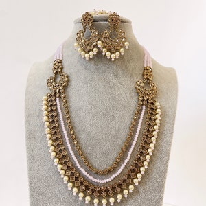 May include: A gold and white layered necklace with pearl accents and matching earrings. The necklace features a delicate design with multiple strands of beads and a pendant.