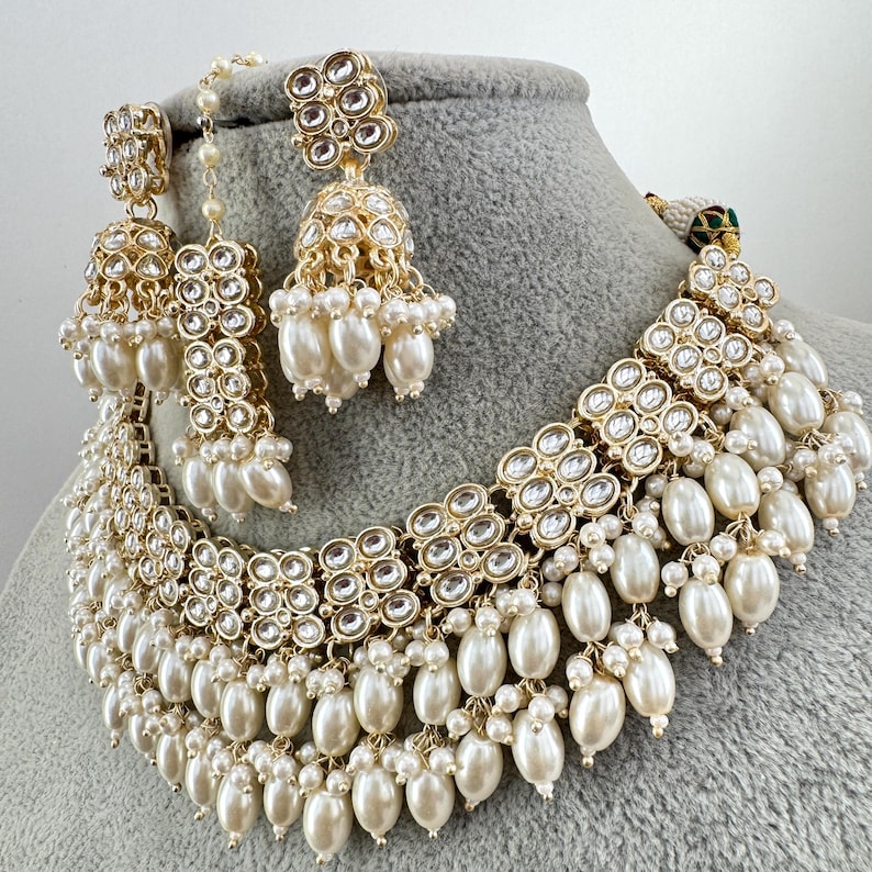 May include: A gold necklace and earrings set with white pearls and clear stones. The necklace has multiple layers of pearls and stones, and the earrings are dangle style.