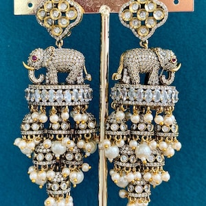 May include: A pair of gold tone earrings with a dangling elephant charm, pearl accents, and clear rhinestones.