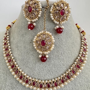 May include: A gold necklace and earrings set with red and white stones. The necklace has a pendant with a red stone in the center. The earrings have a similar design.