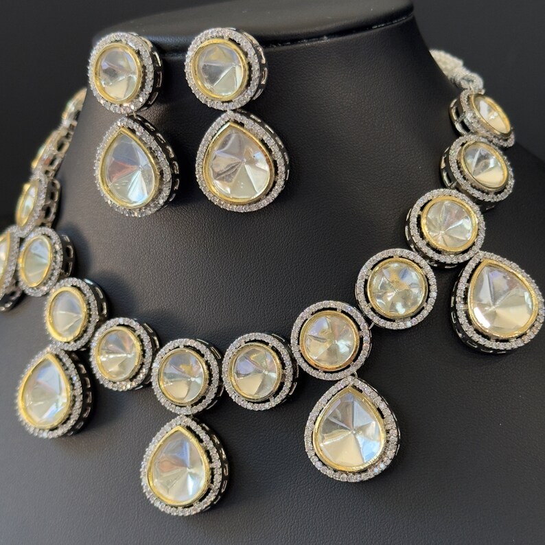 May include: A silver and gold necklace and earrings set with large, clear, teardrop-shaped stones surrounded by smaller, clear stones.