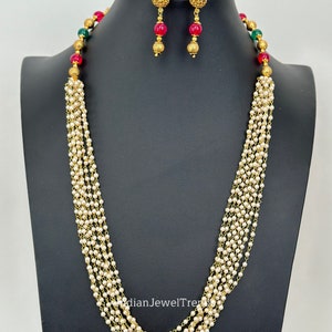 May include: A multi-strand pearl necklace with gold accents and red and green beads. Matching earrings with red and green stones are included.