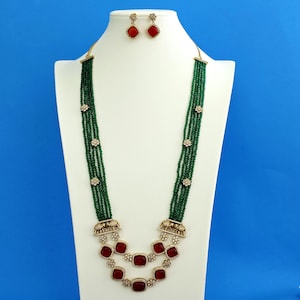 May include: A multi-strand green beaded necklace featuring gold-tone elephant motifs, square red stones, and floral accents, paired with matching square red stone stud earrings on a white display stand.